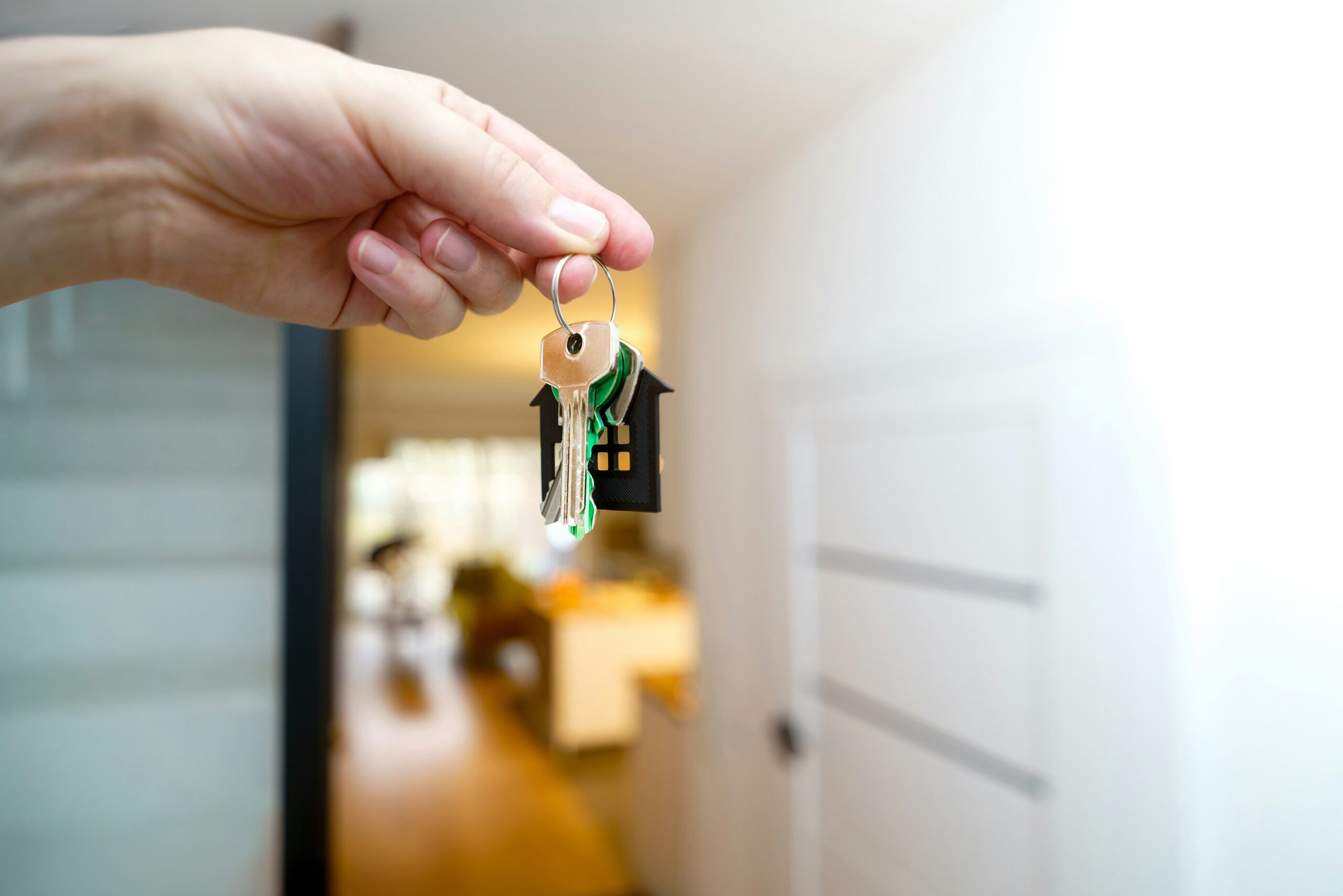 A hand holding a key with an open door background.