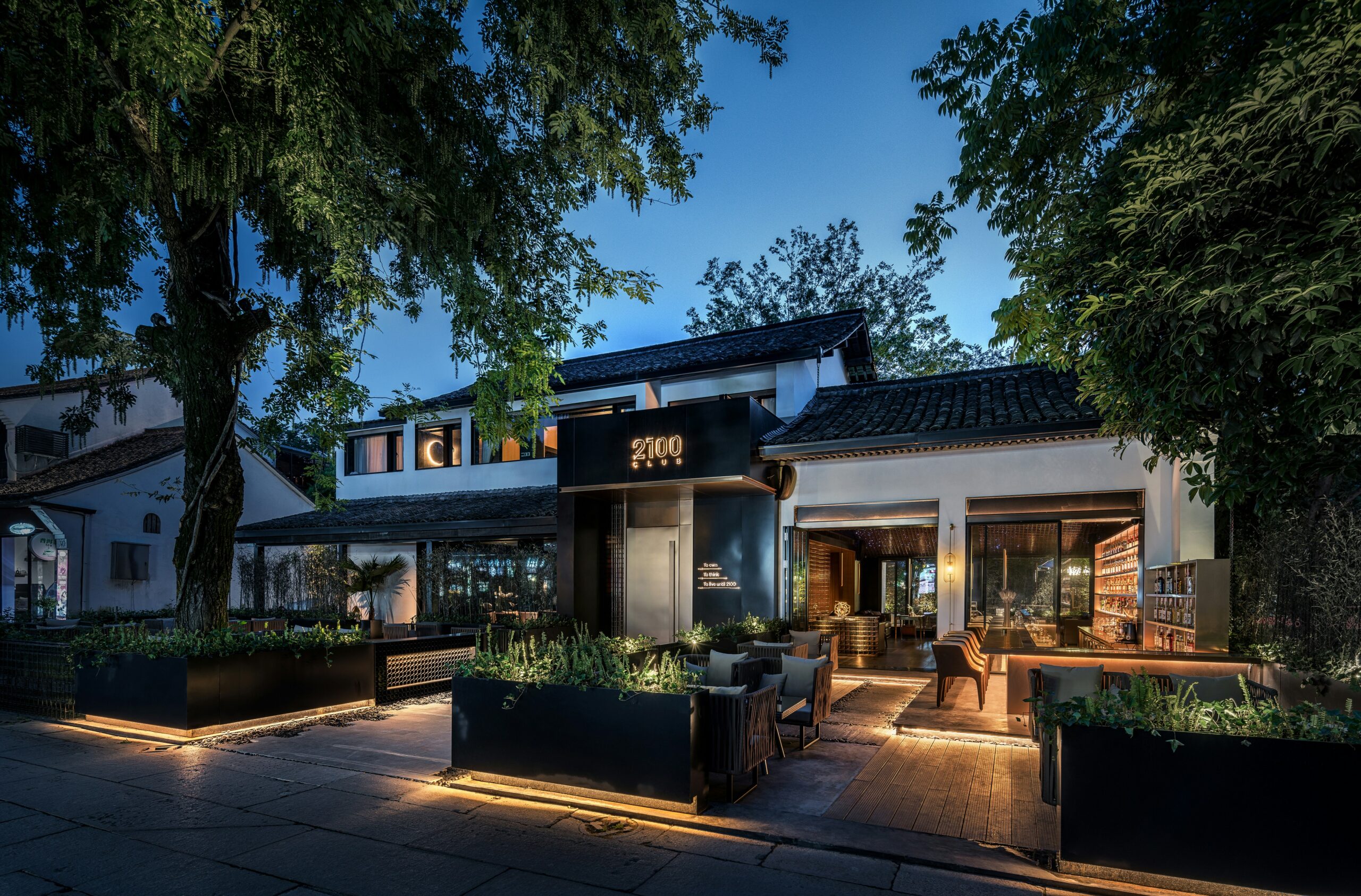 Modern restaurant patio illuminated at dusk with a "2100 club" sign.