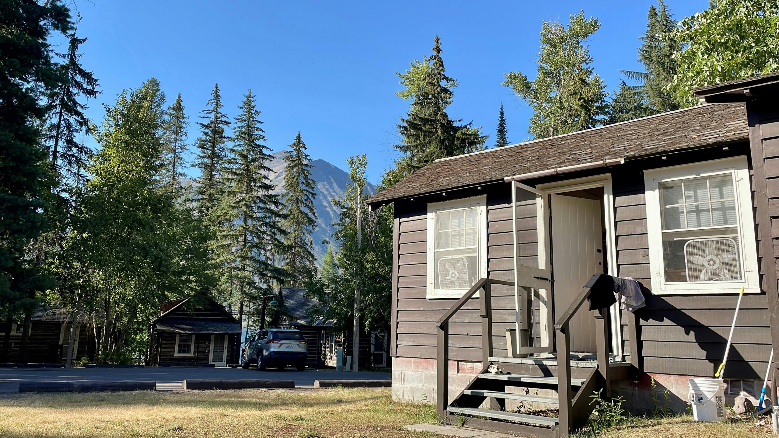 An eye level view of a house near the mountains of Montana with trees and a car in it.