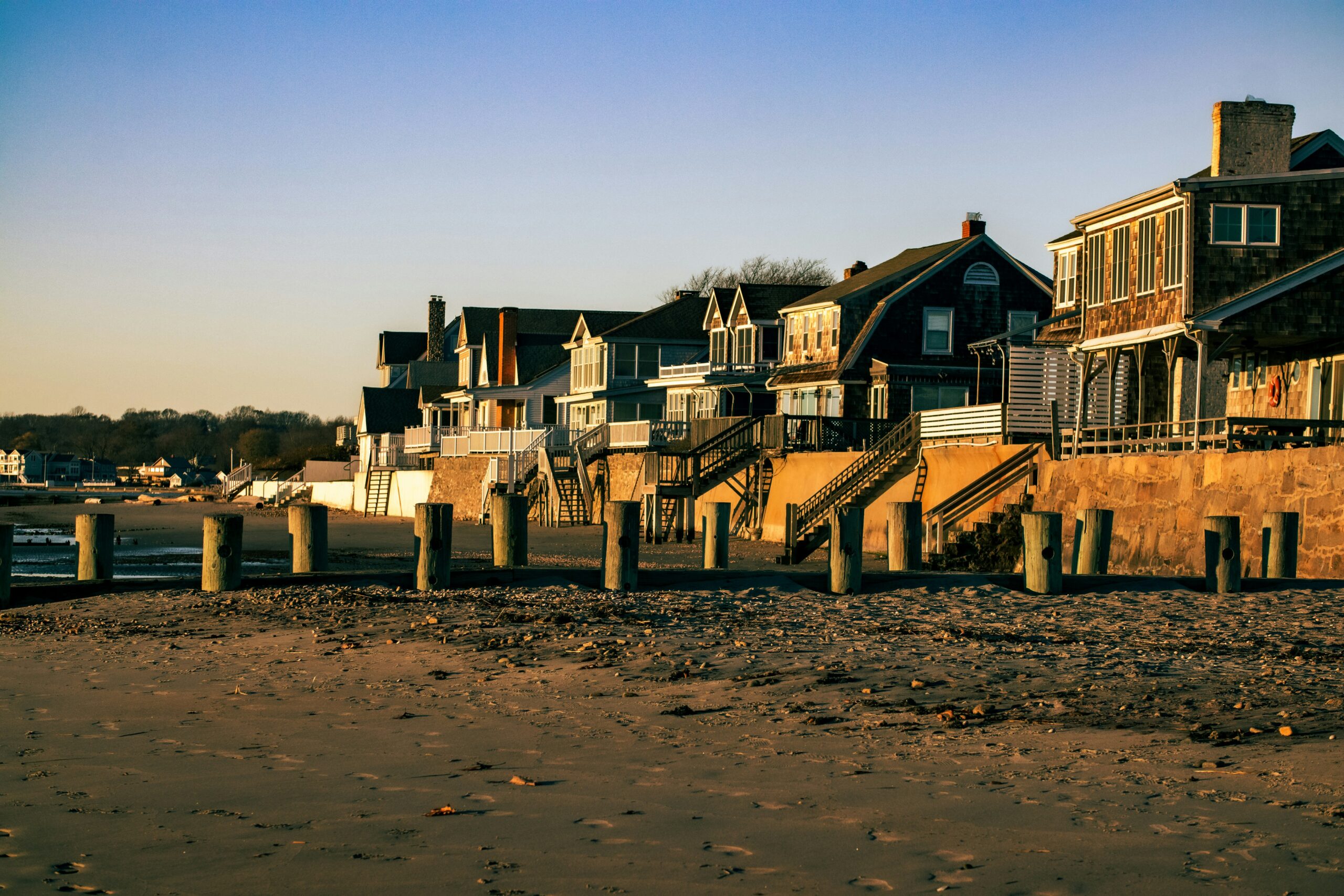 Beachfront houses on stilts along a sandy shore at sunset in Connecticut.