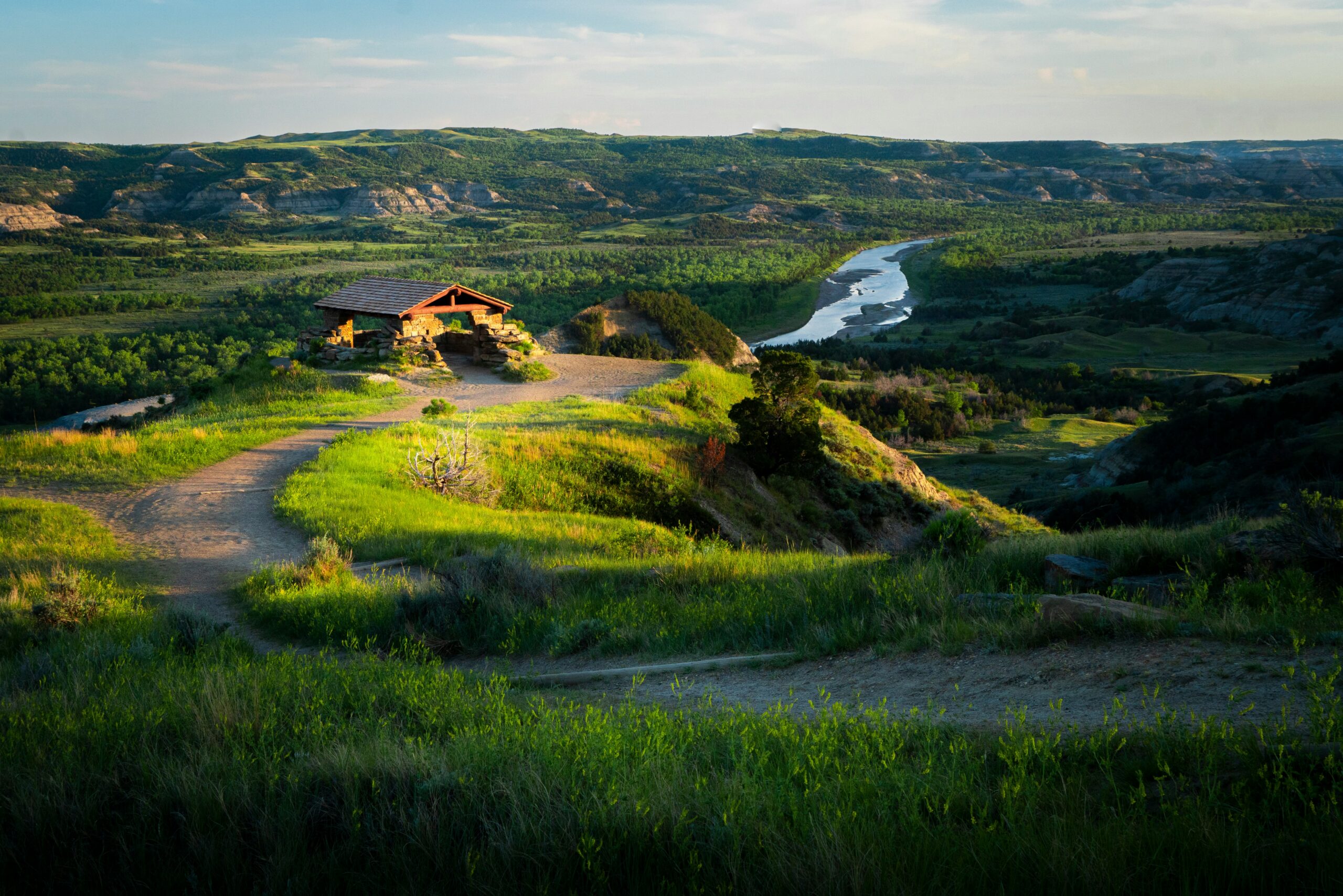 A landscape view of North Dakota with a house, trees, grass and a river.