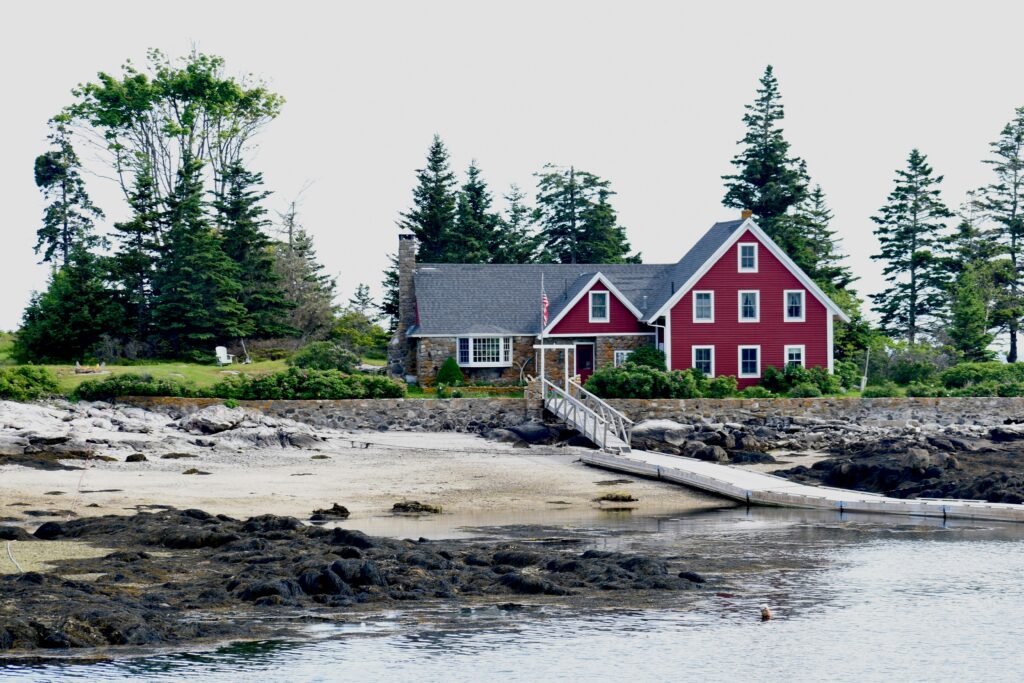 A photo of a house beside a sea in Maine with trees behind it.